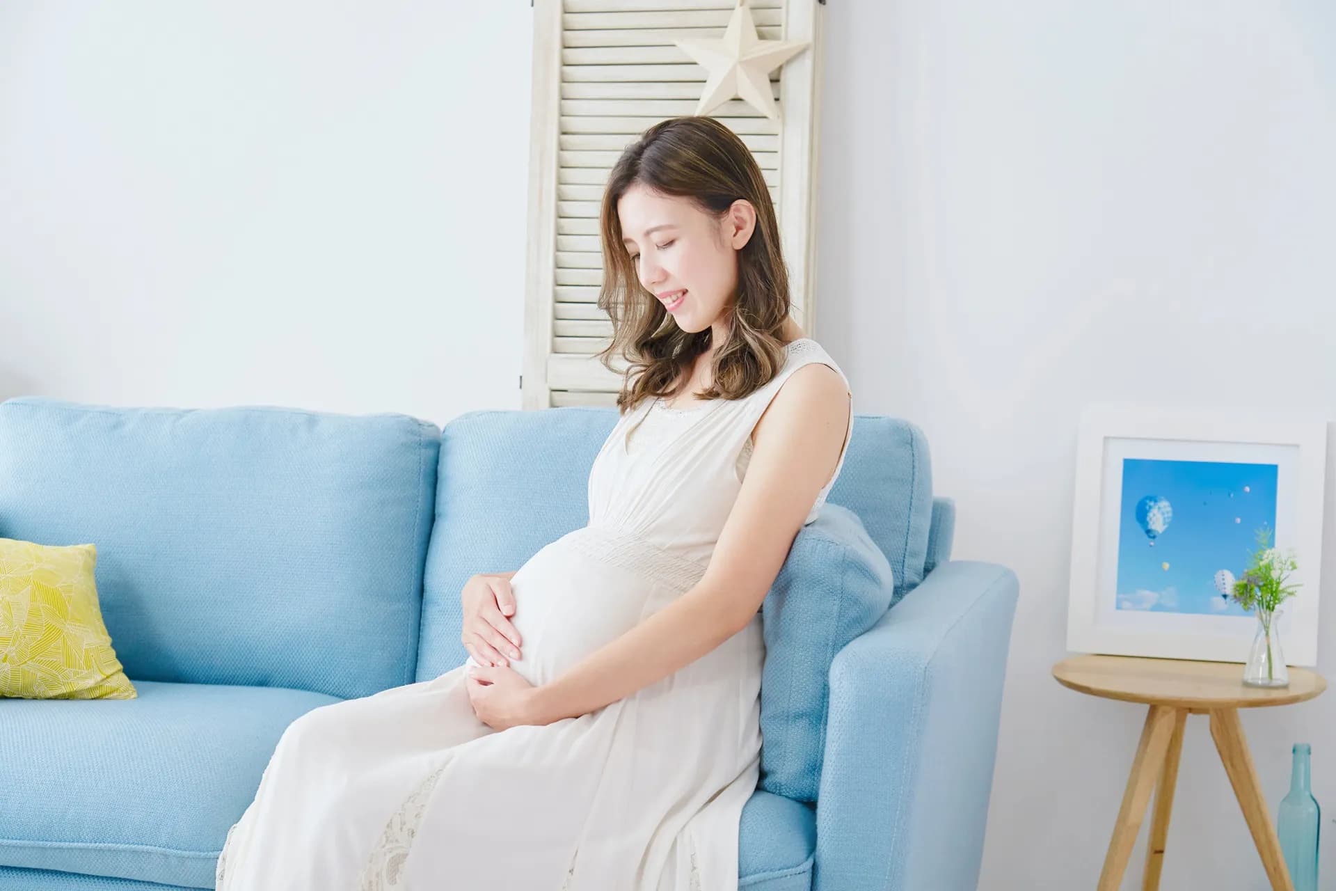 ソファーに座り、お腹に手を添える妊婦